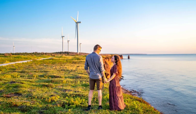Couple overlooking the red cliffs and wind turbines at North Cape, Prince Edward Island during sunset.