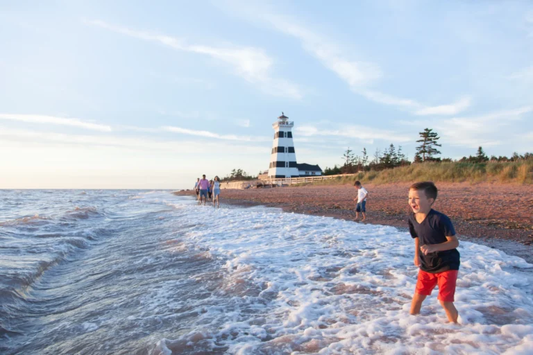 Children playing on the beach with the West Point Lighthouse in the background at sunset in Western Prince Edward Island.